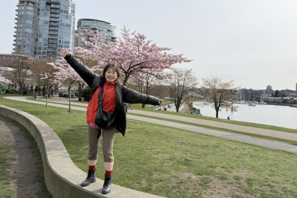 「バンクーバーの満開の桜の下で両手を広げる日本人女性」